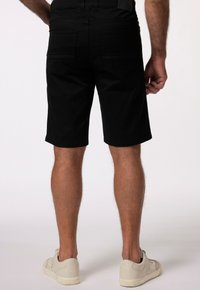 Pantaloni corti neri realizzati in tessuto morbido con una vestibilità dritta, dotati di due tasche posteriori e orlo pulito. Abbinati a sneakers di colore chiaro.