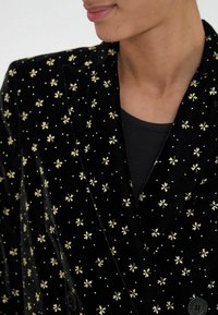 Blazer en velours noir avec broderie florale dorée éparpillée, doté d'un col à revers et d'une fermeture à double bouton.