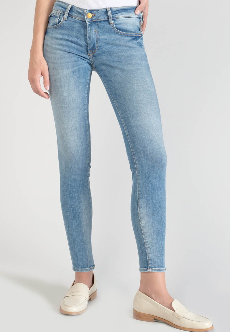 Jean skinny bleu clair déchiré avec cinq poches, une fermeture à bouton jaune et une légère décoloration, associé à des mocassins cream.