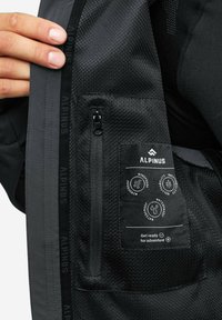 Czarna kurtka wewnętrzna z teksturowanym materiałem, z kieszenią zapinaną na zamek oraz metkami informującymi o odporności na wiatr, oddychalności i wodoodporności.