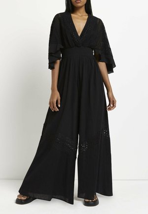 Czarny kombinezon z szerokimi nogawkami, z głębokim dekoltem w kształcie litery V, falbaniastymi rękawami i koronkowymi zdobieniami na dole. Wykonany z teksturowanej tkaniny.