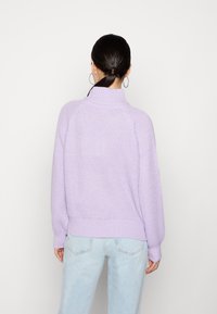 Pull en tricot violet clair avec un col montant, un ourlet côtelé et des manches longues. Porté avec un jean bleu clair, affichant une coupe décontractée.