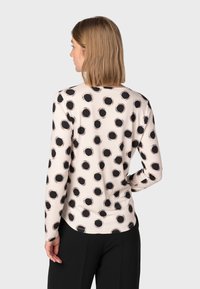 Maglietta a maniche lunghe in tessuto beige chiaro con un motivo circolare nero. Presenta un colletto rotondo e maniche aderenti.