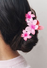 Plastic hair accessory featuring several pink flowers with translucent petals, secured in a dark brown bun, set against a neutral background.