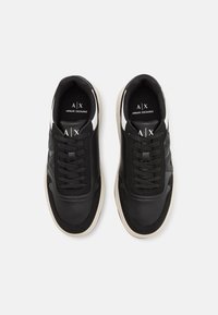 Svarta sneakers med ett texturerat mesh och övre del i slät läder, med svarta snören, en vit sula och en diskret logotyp på tungan.