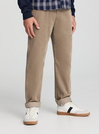 Pantaloni beige in velluto a coste con superficie testurizzata, caratterizzati da risvolti arrotolati e vestibilità comoda, abbinati a sneakers bianche e una camicia a quadri blu navy.