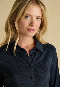 Tmavomodrá blúzka so vzorom leopardieho potlače, s button-down predným zapínaním a klasickým golierom. Mäkká látka s hladkou textúrou.