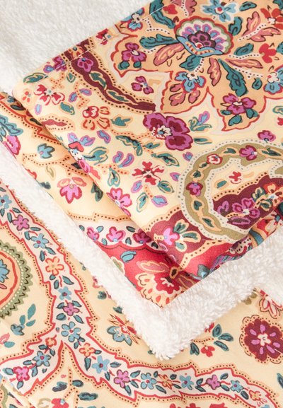 Tissu plié avec des motifs floraux colorés et paisley à côté d'un tissu blanc texturé sur un fond clair.