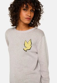 Pull léger gris clair en tissu tricoté doux, avec un design d'oiseau jaune sur la poitrine et un col rond. Texture bouclée visible.