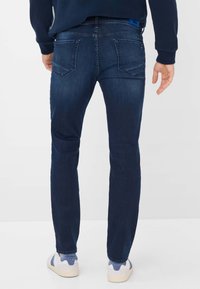 Jeans in denim blu scuro con vestibilità slim, dotati di due tasche posteriori, sbiaditure sottili e una cintura con cuciture e etichetta del marchio.