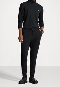 Svart polo tröja med en liten logga, tillsammans med svarta joggarbyxor med elastisk midja och dragsko. Sneakers kompletterar outfiten.