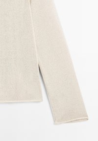 Jasno beżowy sweter robiony na drutach z długimi rękawami, z teksturowanym, otwartym splotem. Bocznie rozcięte na ćwierć długości u dołu. Prosty krój, bez ozdób.