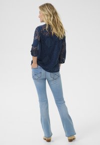 Top de encaje navy con patrones circulares, mangas tres cuartos, combinado con jeans de campana azul claro y botas de tacón color caramelo.