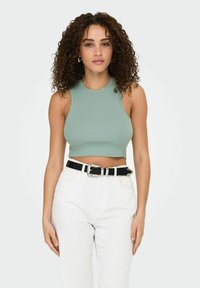 Mintgroene geribbelde mouwloze crop top gecombineerd met hoge witte jeans en een zwarte riem met een zilveren gesp.