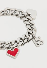 Ασημένιο βραχιόλι αλυσίδας με κόκκινο μενταγιόν σε σχήμα καρδιάς και τετράγωνο μενταγιόν, με ετικέτα "HUGO" προσαρμοσμένη στην αλυσίδα.