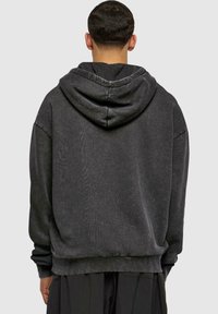 Sudadera gris oscuro con una textura suave, gran capucha y hombros caídos. Presenta un corte relajado y puños acanalados.