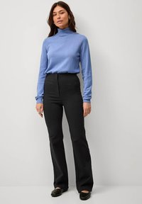 Lichtblauwe coltrui, zwarte flared broek en zwarte instappers. Glad materiaal met een getailleerde pasvorm en minimale details.