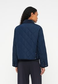 Casaco acolchoado azul marinho com gola, apresentando botões de pressão metálicos nas laterais, tecido texturizado e um design cropped.