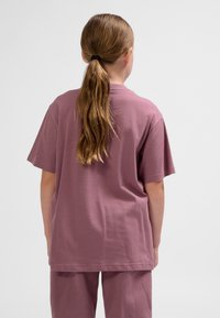 Kortärmad, ljus mauve t-shirt i bomull med avslappnad passform och rundad halsringning, sedd bakifrån med matchande byxor.