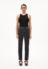 Zwart geribbelde tanktop, high-waisted donkere jeans en zwarte ballerina's met decoratieve gespen. Rechte pijpen en minimalistische stijl.
