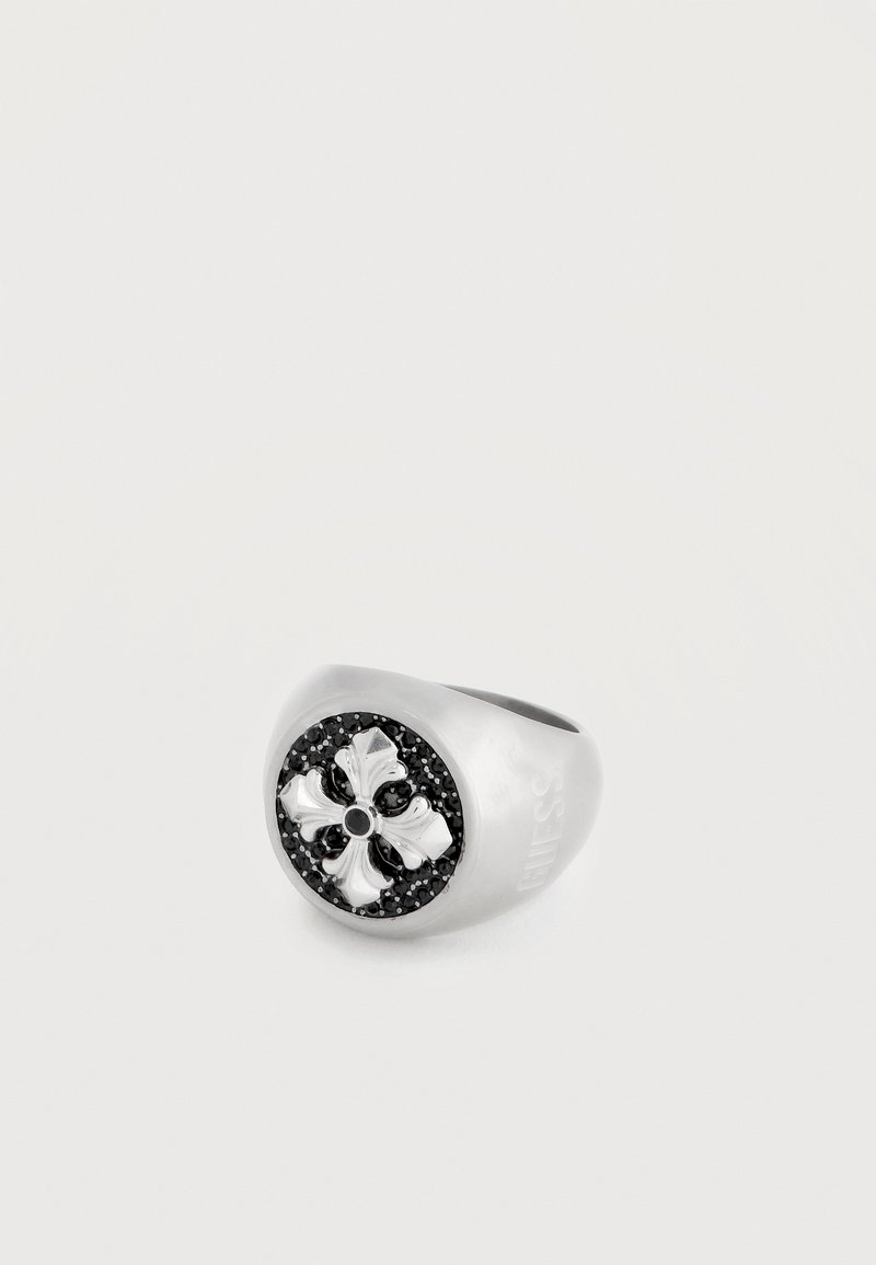 Bague en argent avec un centre circulaire noir présentant un motif floral à quatre pétales en relief, entouré de petites pierres noires.