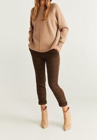 Maglione beige a maglia con texture a coste, abbinato a pantaloni a quadri marroni tapered e stivaletti crema con punta affusolata e bordi scallop.