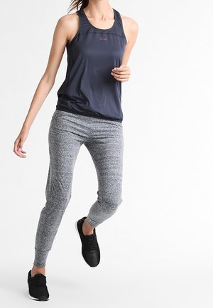 Haut de sport sans manches gris foncé associé à un pantalon de jogging gris clair chiné. Le tissu semble léger. Chaussures de sport noires avec des détails texturés.