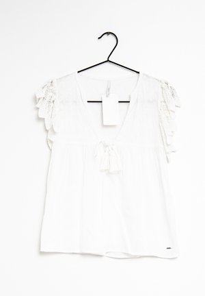 Weiße Bluse mit kurzen Spitzenärmeln, tiefem V-Ausschnitt, Quastenband und einem weißen Etikett, das an einem schwarzen Kleiderbügel vor weißem Hintergrund hängt.