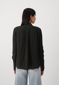Svart langermet skjorte med krage og løs passform, med en ryggsøm, iført over lyseblå vide denimjeans.
