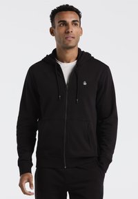 Zwarte rits hoodie met een voorzak, verstelbare trekkoorden en een klein logo op de borst. Gemaakt van een zachte, textuurstof.