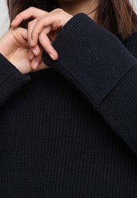 Námořnický pletený svetr s dlouhými rukávy, který má oversized manžety. Pletená struktura je výrazná a ukazuje na jemnou, silnou látku.