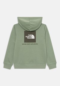 Fleece verde com bolso tipo canguru, textura suave e punhos canelados. Apresenta um grande logótipo em preto e branco nas costas, com texto abaixo.
