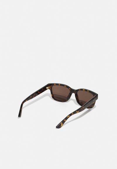 Ochelari de soare tortoise cu un design pătrat, lentile maronii și rame groase. Accentele din aur de pe lateral adaugă un detaliu.