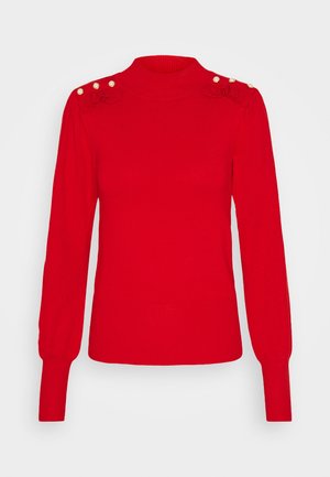 Pull en maille rouge à manches longues avec poignets et ourlet côtelés, col montant et détails de boutons en perle sur les épaules avec accents à volants.
