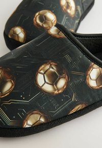 Čierne šľapky s lesklým vzorom zlatých futbalových loptičiek na pozadí pripomínajúcom obvod, s jemnou textúrovanou podšívkou.