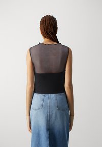 Svart ermeløs topp med gjennomsiktig bak, scalloped halslinje, paret med en denimskjørt med lommer og full passform.