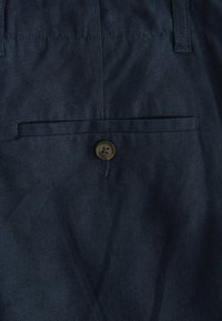 Pantaloni din țesătură albastru închis, având un buzunar posterior cu un singur buton maro, textură netedă și detalii de coasere ajustate.