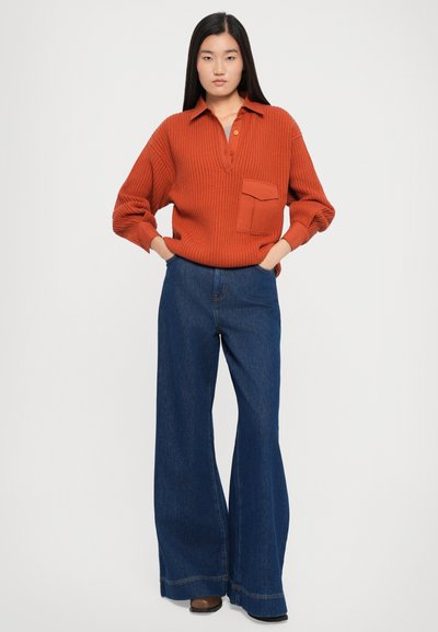 Ribbed rust-colored sweater with a collar and pocket paired with wide-leg dark denim jeans featuring a raw hem and brown heeled boots.