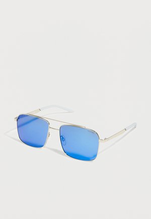 Lunettes de soleil élégantes avec fines montures en métal doré et verres carrés miroirs bleus reposant sur une surface blanche.