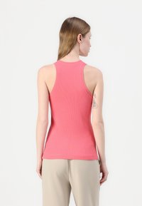 Tettsittende rosa ribbestrikket tanktopp med rund halsutskjæring og racerback-design, kombinert med lyse bukser som viser en glatt tekstur.