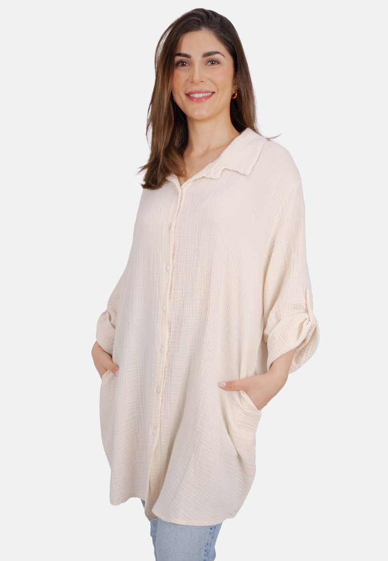 Helles beiges Hemd mit knopfverschluss in lockerer Passform, aus strukturiertem Stoff. Mit einem klassischen Kragen und zwei seitlichen Taschen. Die langen Ärmel können hochgerollt werden.