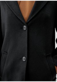 Svart jacka i ullblandning med nedhasad krage, två knappar och sidofickor; mjuk textur med slät yta.