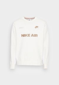Vit Nike sweatshirt med rund halsringning, med "NIKE AIR" i beige tryck och subtila varumärkesdetaljer på bröstet. Mjuk textur.