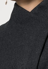 Tessuto di lana grigio scuro con una finitura testurizzata, caratterizzato da un design del colletto alto e angolare. I dettagli delle cuciture aggiungono un sottile interesse visivo.