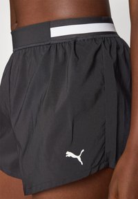 Svarta sportshorts gjorda av lättviktsmaterial. Har en vit rand på det elastiska midjebandet och en liten vit logotyp på sidan.