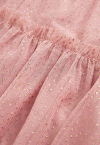 Tissu rose doux avec de fines paillettes dorées et des coutures froncées créant des sections texturées et volantées.