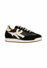 Zwarte en crèmekleurige sneaker van suede en leder, met een zigzagpatroon en lichtbeige veters, een witte zool en textuuraccenten.