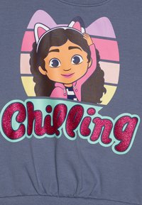 Sweatshirt cinza com um personagem de cartoon com cabelo encaracolado, vestindo uma jaqueta rosa e orelhas de gato, com a palavra "Chilling" em letras brilhantes rosas.