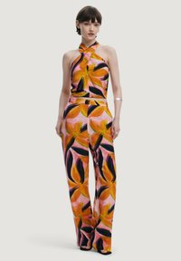 Completo a due pezzi con top a collo alto e pantaloni a gamba larga, su uno sfondo rosa decorato con audaci motivi floreali arancioni e neri.