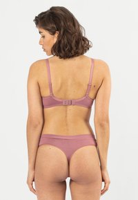 Pinke Lingerie-Set mit einem Bralette mit verstellbaren Trägern und Hakenverschluss, kombiniert mit passenden Mid-Rise-Slips, glatte Textur.